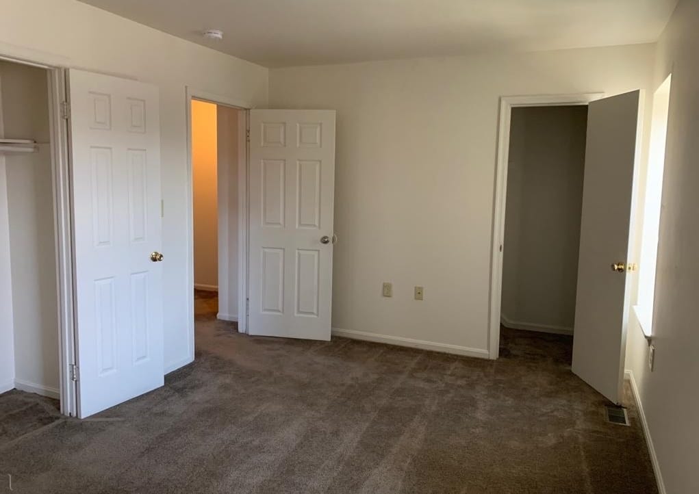 A carpeted bedroom in a Thurmont Village townhouse with a reach-in closet and a doorway to the hall