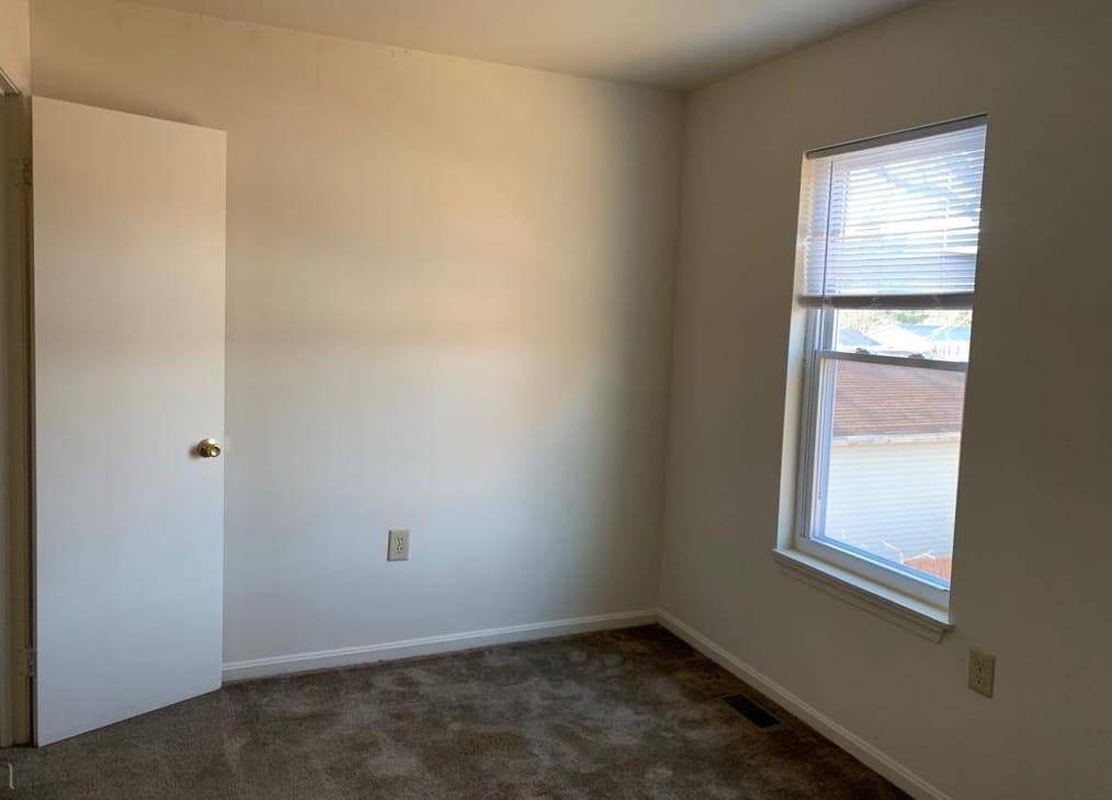 A bright carpeted bedroom at Thurmont Village with a window overlooking the neighboring rooftops