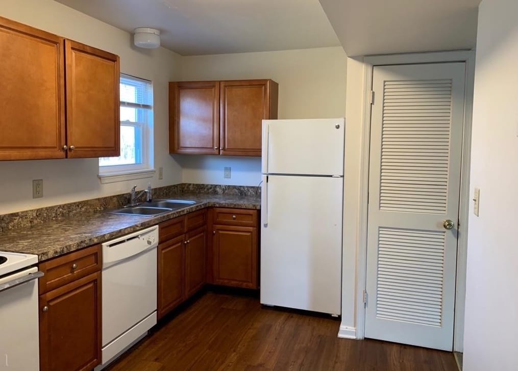 The kitchen in a Thurmont Village townhouse, with wood cabinets, a white refrigerator, a dishwasher, and a dark hardwood floor