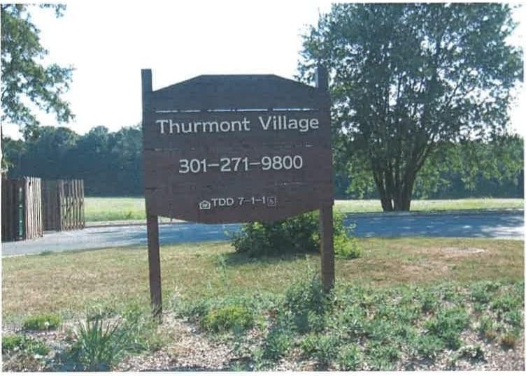The Thurmont Village entrance sign on wooden posts, with an open field and trees behind