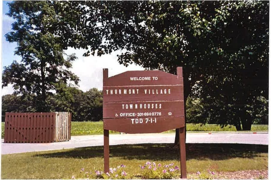 A wooden "Welcome to Thurmont Village Townhouses" sign among shade trees at the community entrance